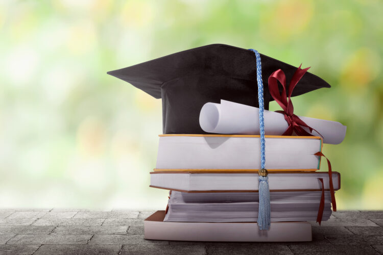 Graduation hat with degree paper on a stack of book against blurred background